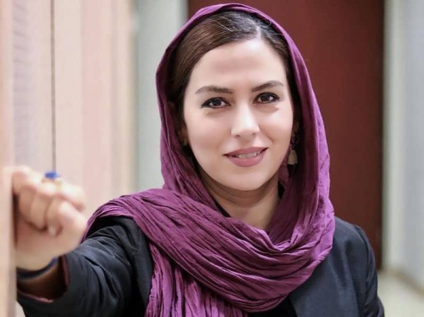 تینا پاکروان با روسری بنفش رنگش به دیوار تکیه داده و به دوربین نگاه می کند